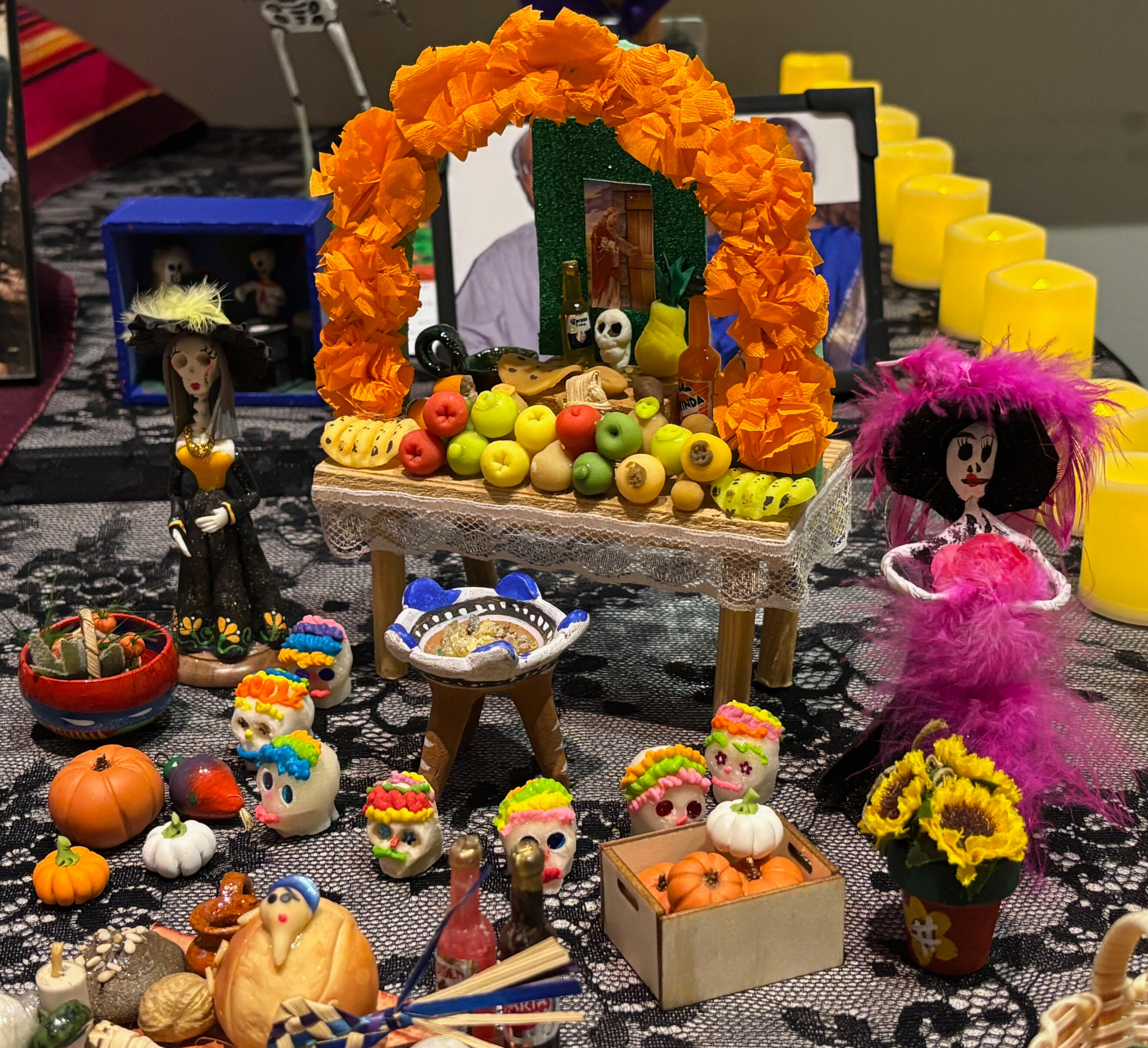 A miniature altar surrounded by well-dressed skeleton figures rests on top of the community altar or ofrenda decorated with black lace and candles. Photo by Bryné Hadnott, The Guardsman